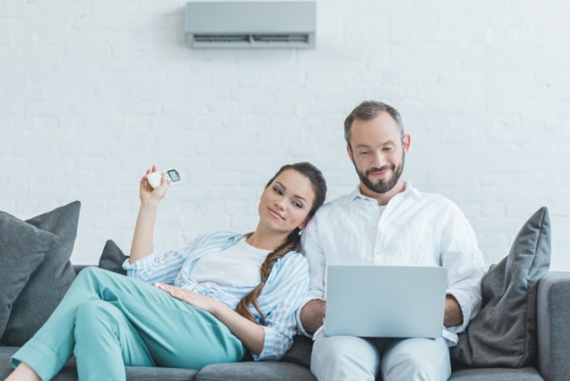 couple sitting on a couch while using a remote to adjust their ductless unit.