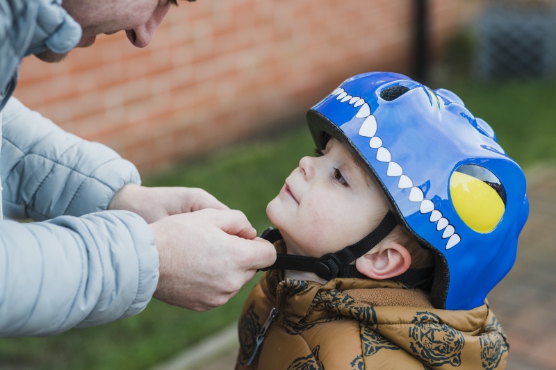 A father fastens his son's safety helmet before going out to play he is making sure it's safely fastened to protect him.