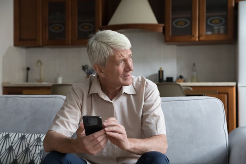 What’s That Smell Coming From My Furnace? Photo of a man on his couch, looking out a window seemingly concerned on his phone.