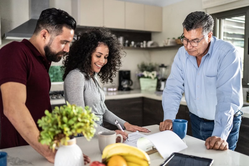 Think HVAC During Your Home Remodeling. Image is a photograph of two men and one woman around a kitchen island reviewing renovation plans.