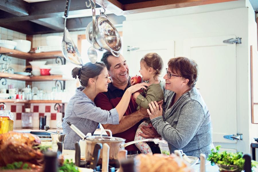 Top 10 Ways to Reduce Your Energy Bill in 2023. Image shows family of four enjoying time together in a kitchen.